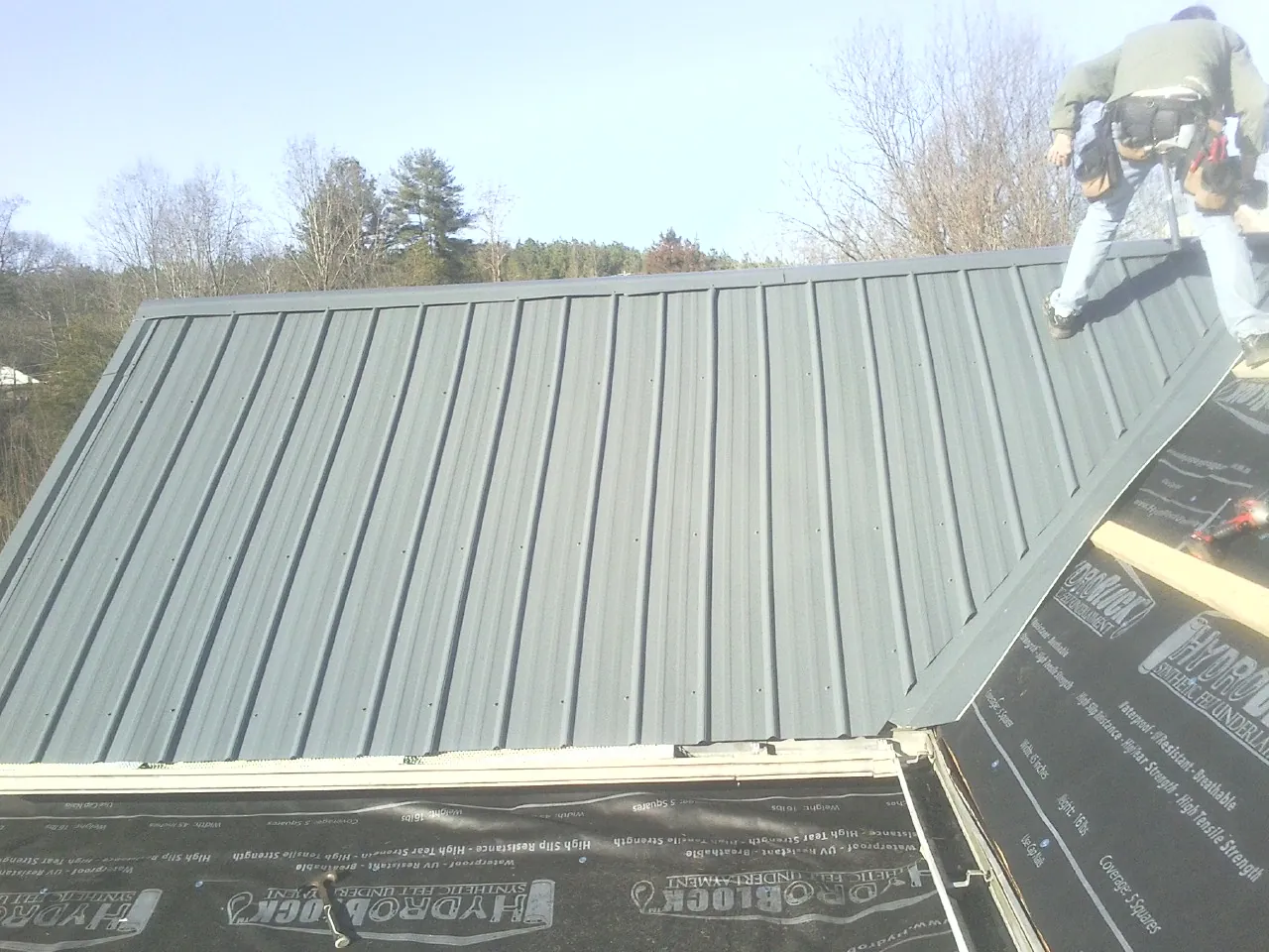 Crew installing dark green standing seam panels over synthetic underlayment in Hawthorne