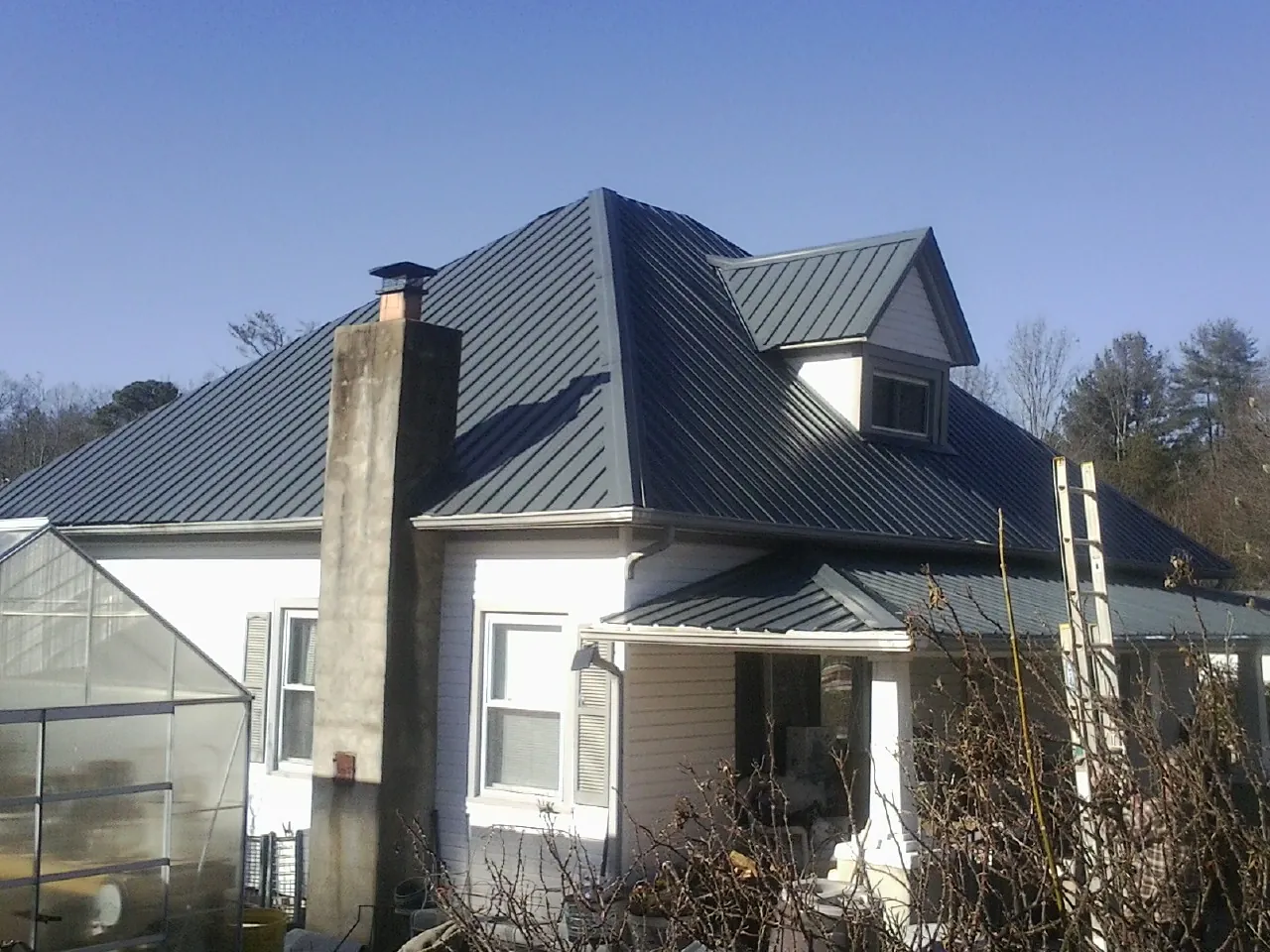 Dark blue standing seam metal roof on a white farmhouse with dormer — Slate & Tile Roof Repair by Roofing Brothers in Hawthorne